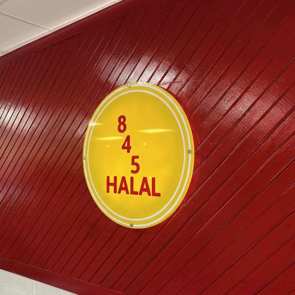 Yellow oval sign reading “845 HALAL” mounted on a glossy red diagonally paneled restaurant wall.