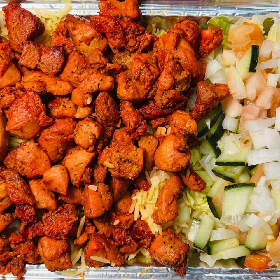 Aluminum tray filled with orange-spiced fried chicken pieces, shredded lettuce, cucumbers, tomatoes, onions, and cheese.