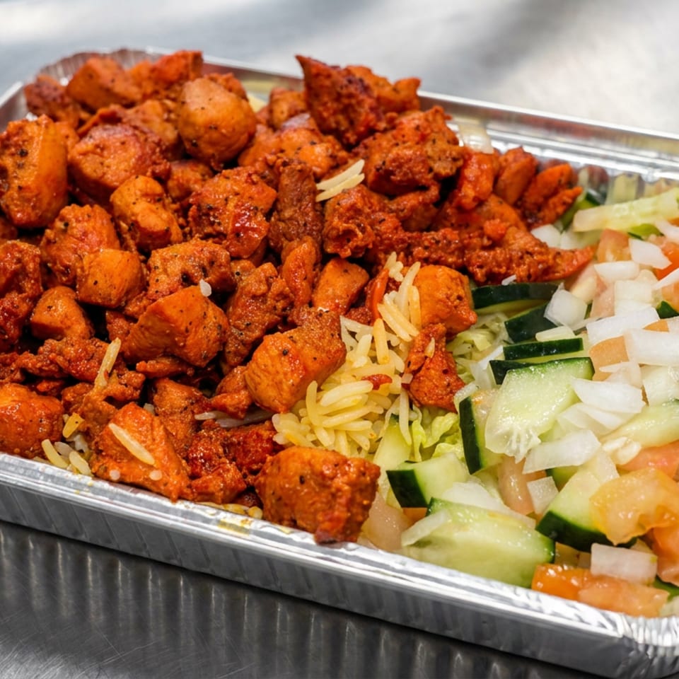 Aluminum tray filled with crispy spiced chicken, yellow rice, and chopped cucumber, lettuce, tomato, and onion salad.